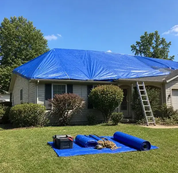 Blue roof tarp secured over a house with a ladder and spare tarps on the lawn in Kaukauna, WI